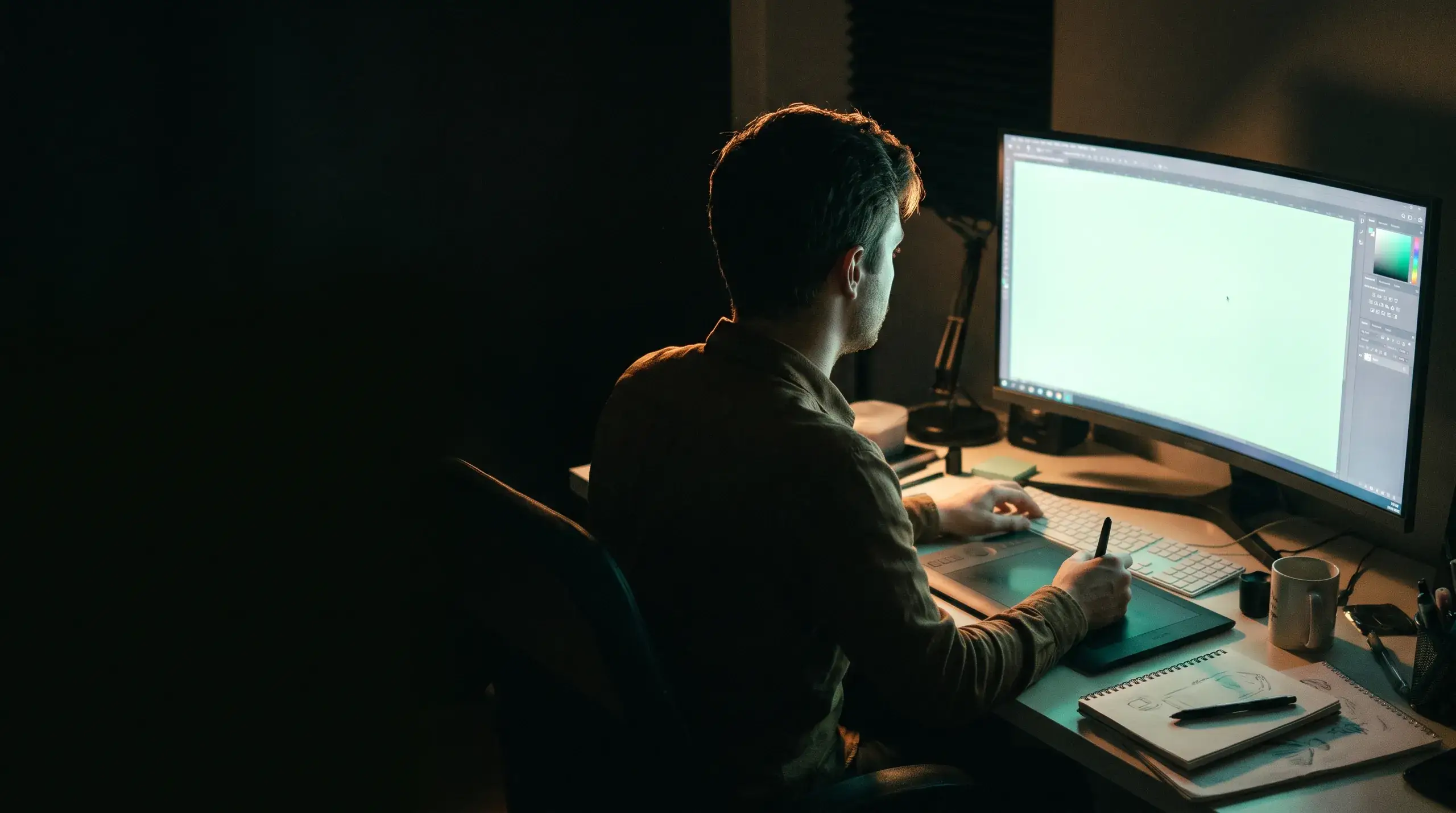 A designer working late at a large monitor with a drawing tablet.