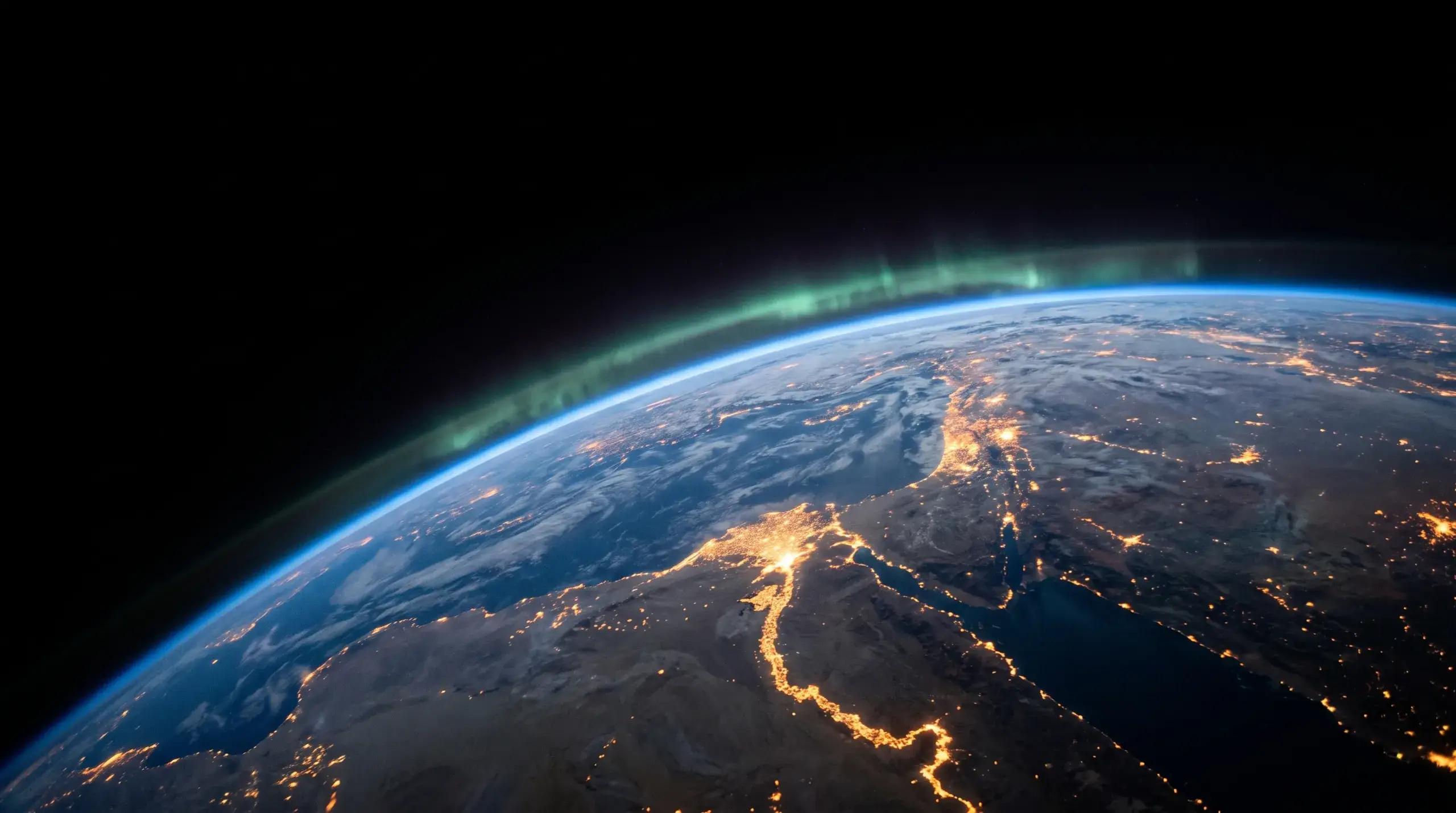 The earth at night seen from orbit, city lights tracing the coastlines.